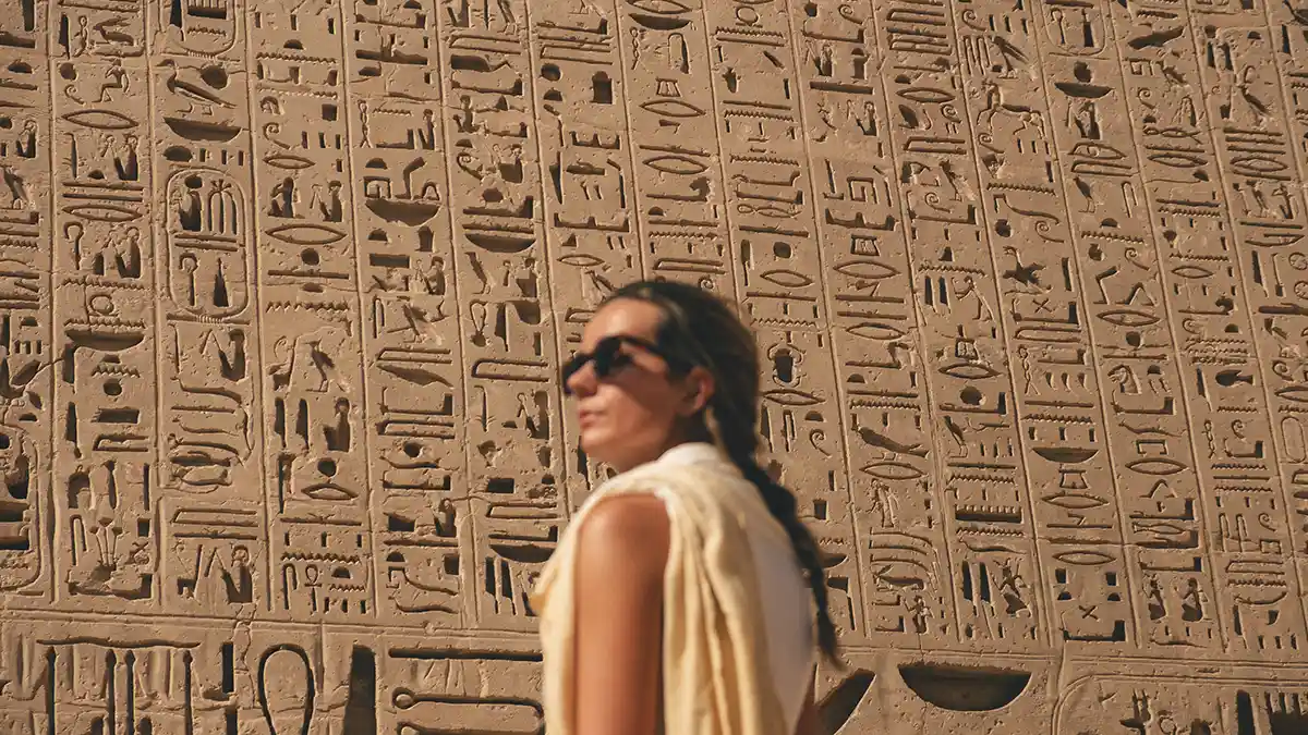 lucy-hieroglyphics Lucy out of focus with a wall in the background which has deep hieroglyphic carvings.