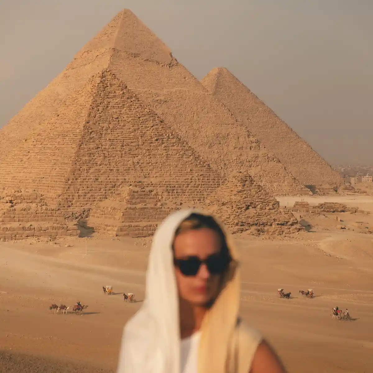 lucy-pyramids-home Lucy standing out of focus while wearing a head scarf and sunglasses with the six pyramids of Giza in the background.