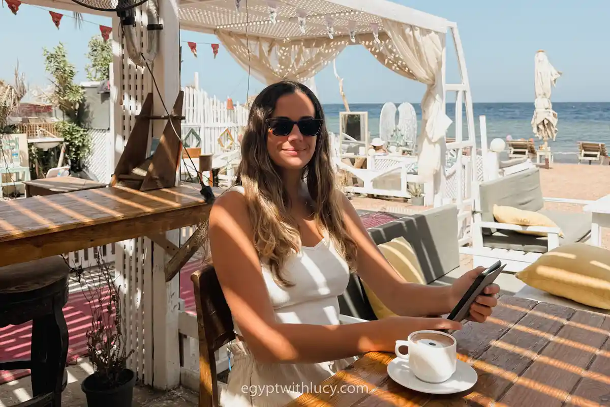 Lucy holds a phone at a wooden table next to a cup at Flat White cafe.