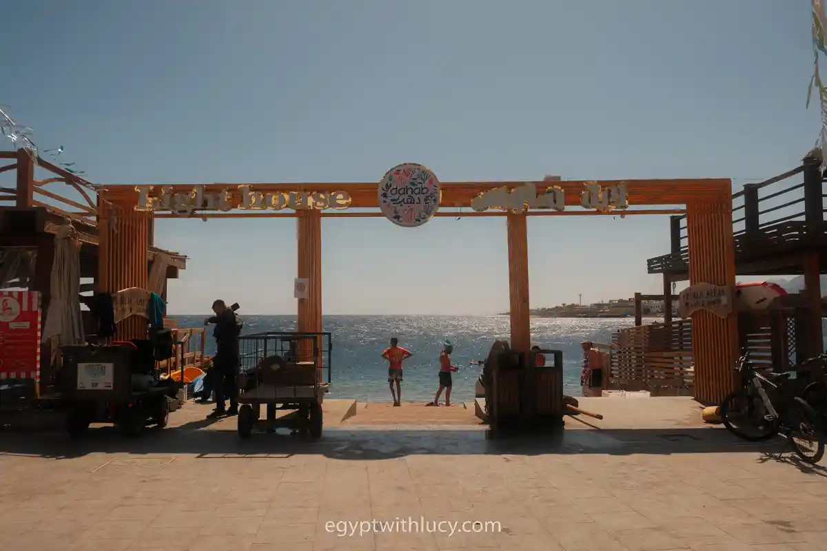 A wooden archway spans across an open entrance leading toward the Lighthouse Bay in Dahab.