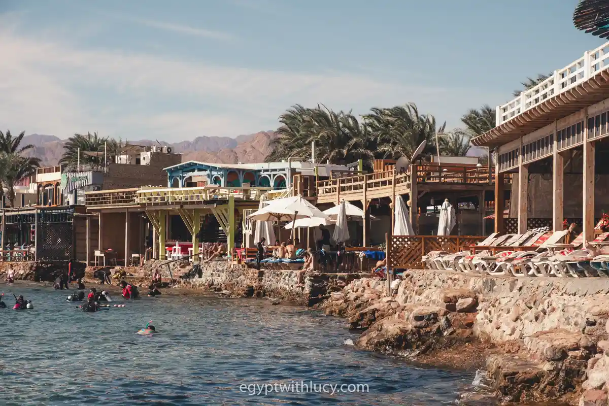 Sun loungers and white umbrellas line a stone wall next to the water at Lighthouse Bay.