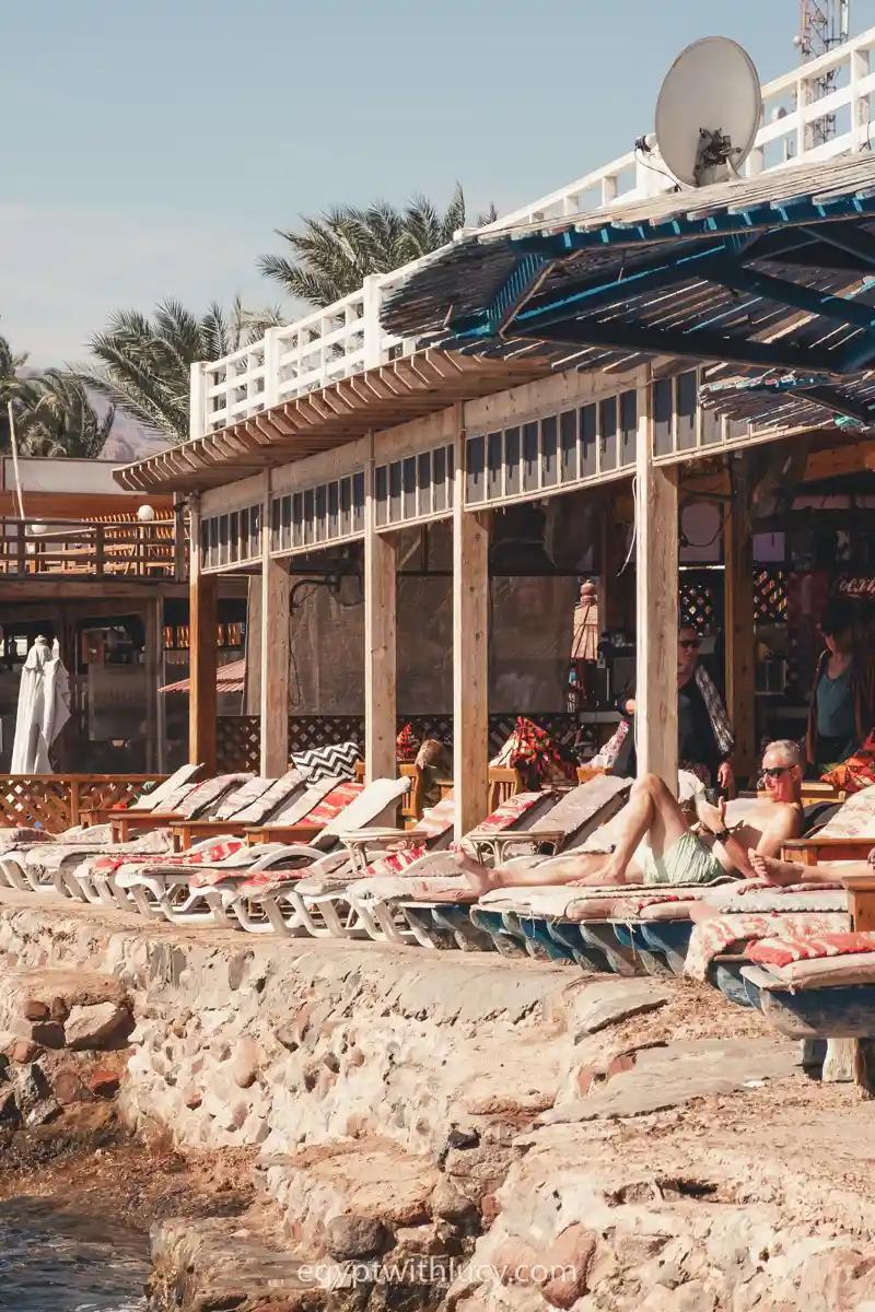 People recline on sun loungers along a rocky stone wall next to Lighthouse Bay.