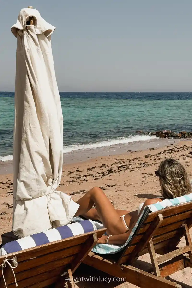 Lucy sunbaths on a wooden lounger with a white umbrella at Dive Urge Beach.