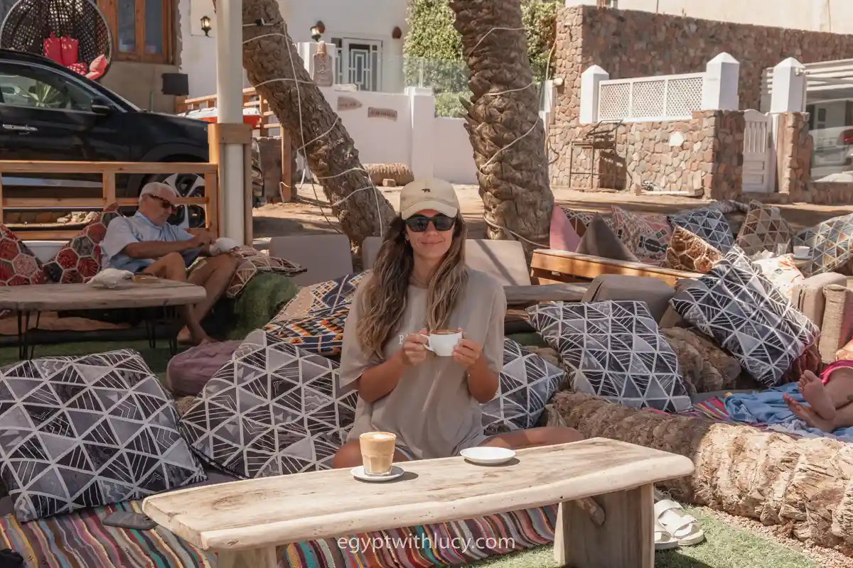 Lucy sits among patterned cushions holding a coffee cup at Neom.