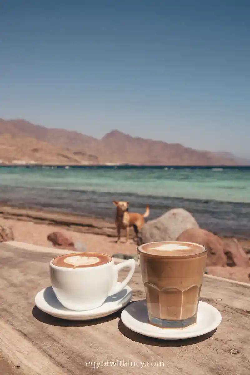Two coffee cups rest on a wooden ledge facing the ocean in front of Neom cafe.