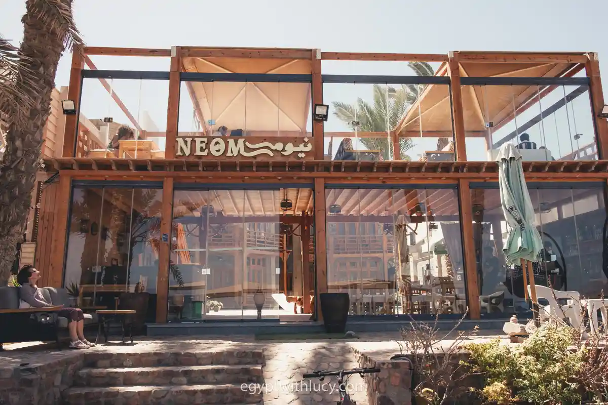 A multi-story glass and wood hotel front stands beneath a sign for Neom written in English and Arabic.