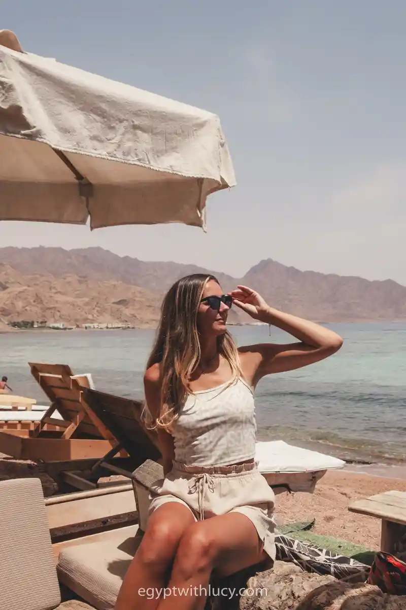 Lucy sits on a lounger beneath a white umbrella at Neom Hotel's beach.