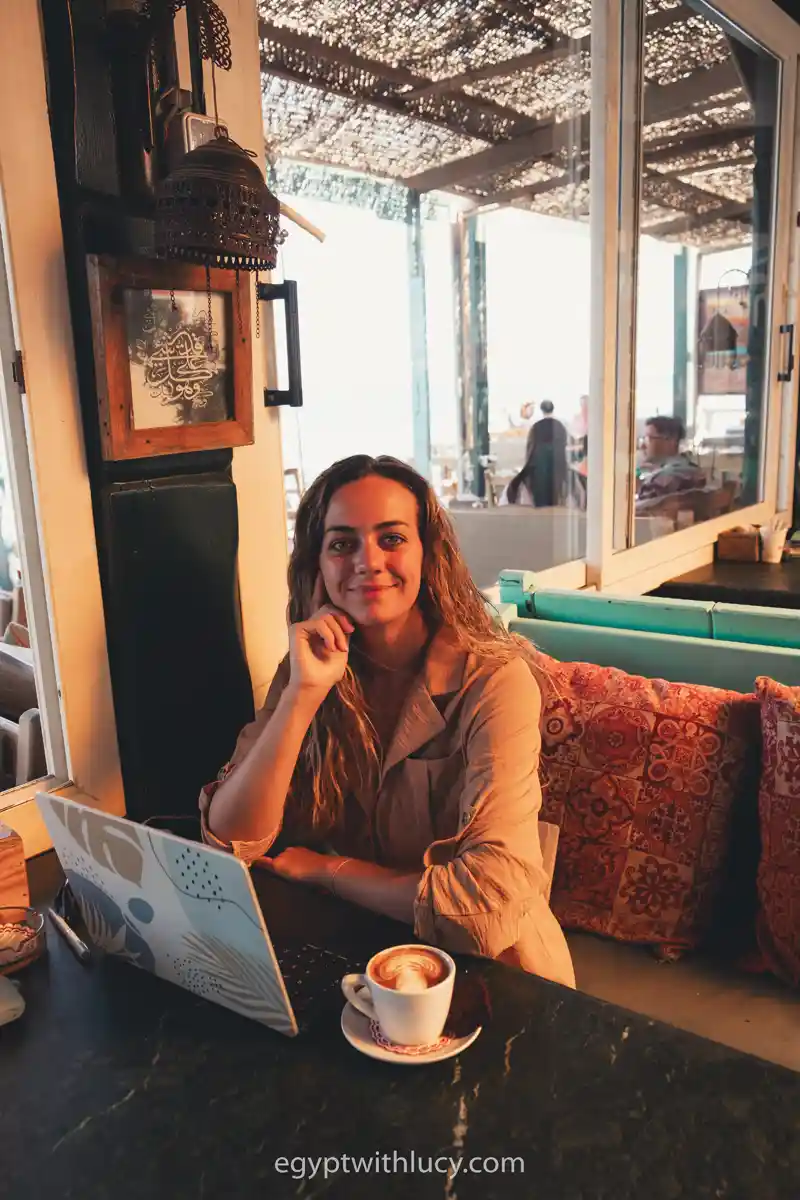 Lucy sits at a table with a laptop and a coffee cup inside Old Everyday Cafe.