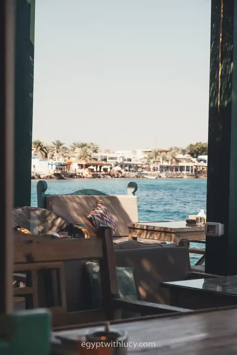 Wooden tables and cushioned seating face the water outside Old Everyday Cafe.