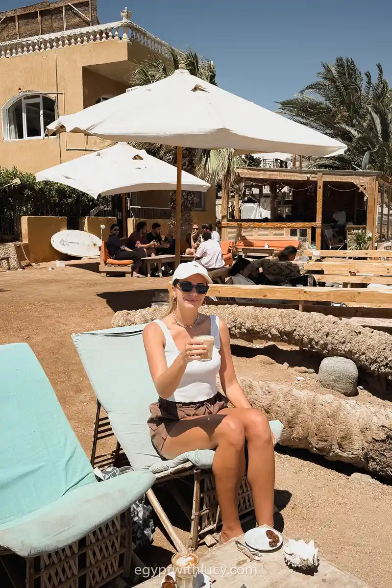 Lucy sits on a lounge chair holding a coffee glass at Sarda Cafe.