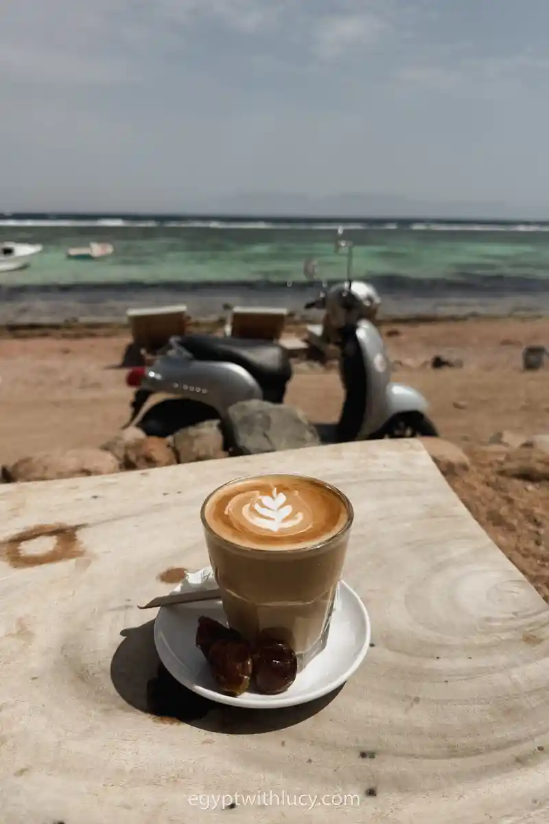 A cup of coffee rests on a saucer on a wooden table at Sarda Cafe.