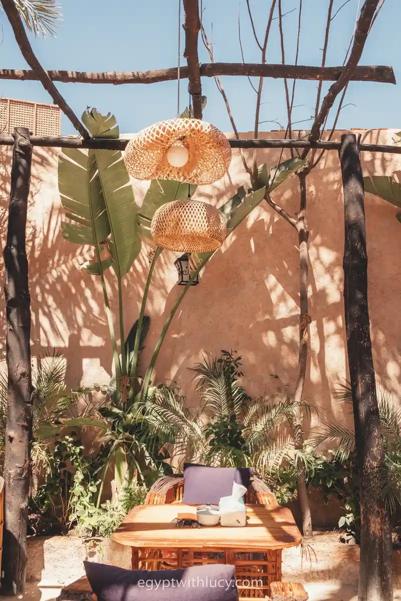 Woven lamp shades hang above a wooden table and green plants at Shanti Cafe.