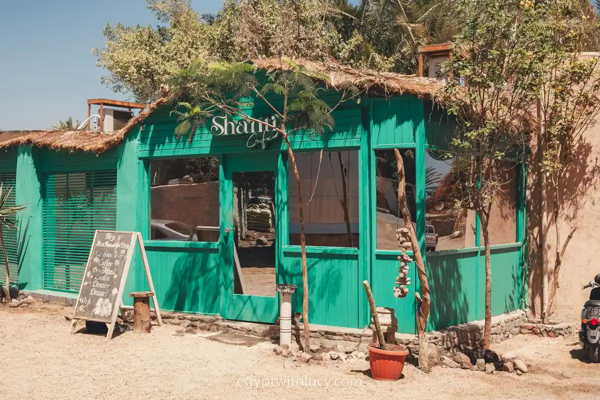 A green wooden building with reflecting windows beneath a sign for Shanti Cafe.