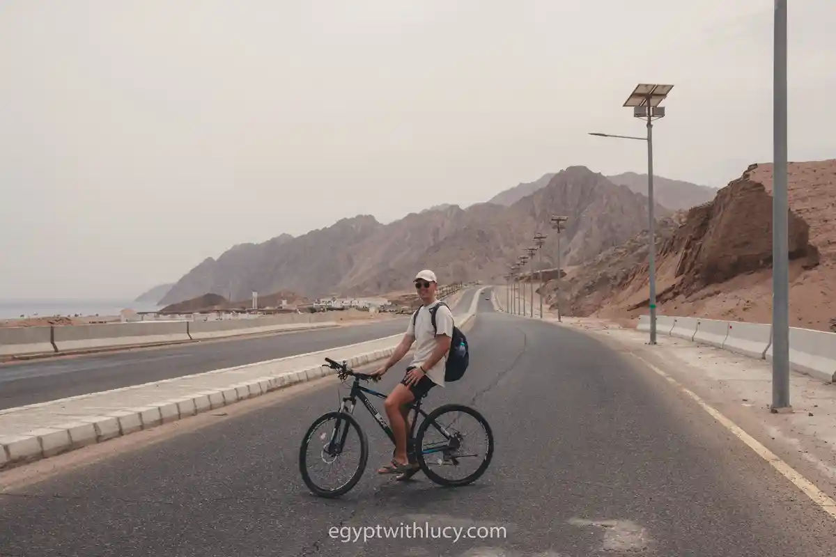 A cyclist in a white cap riding a bicycle on a paved mountain road.