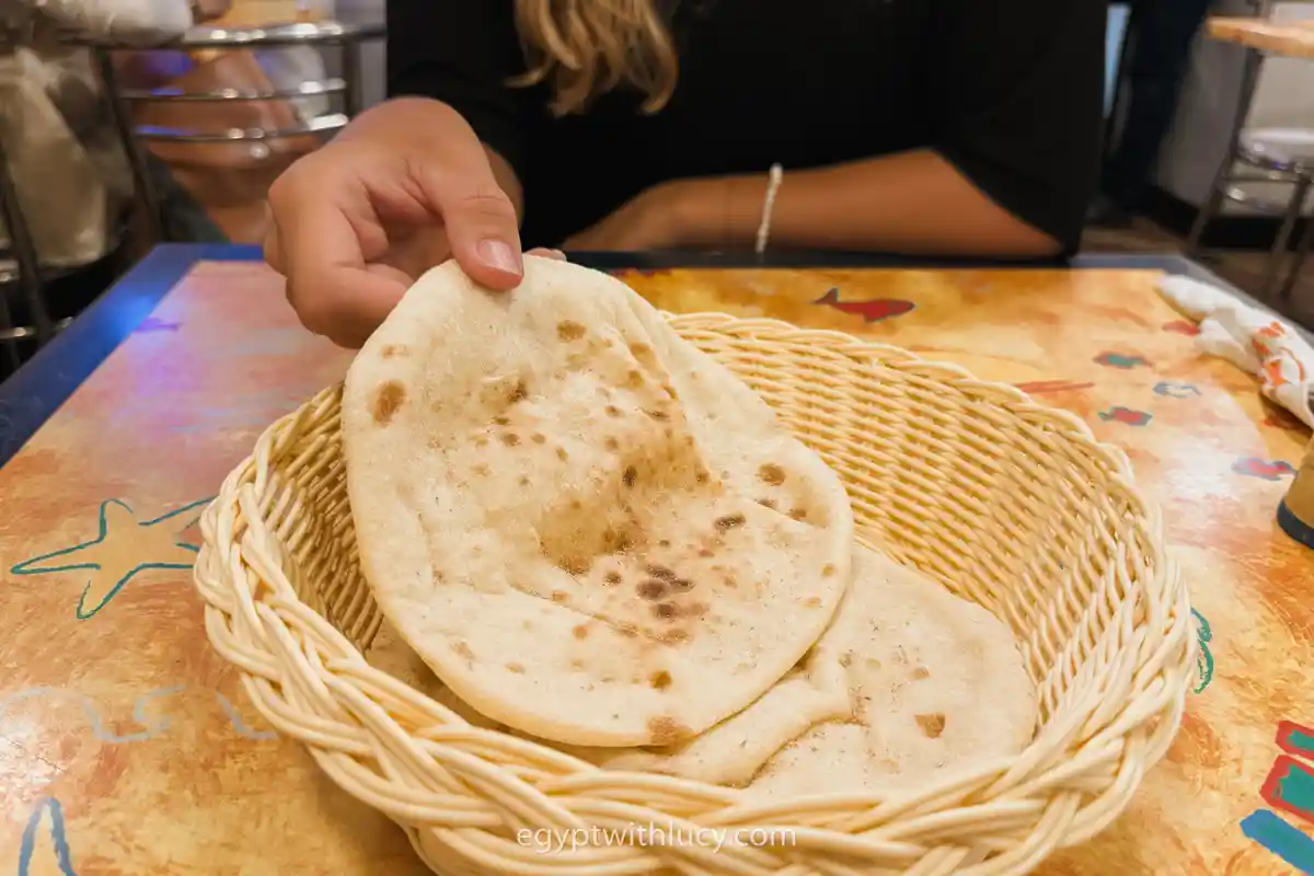 egyptian-bread A hand lifting a round piece of flat Egyptian bread from a woven basket.