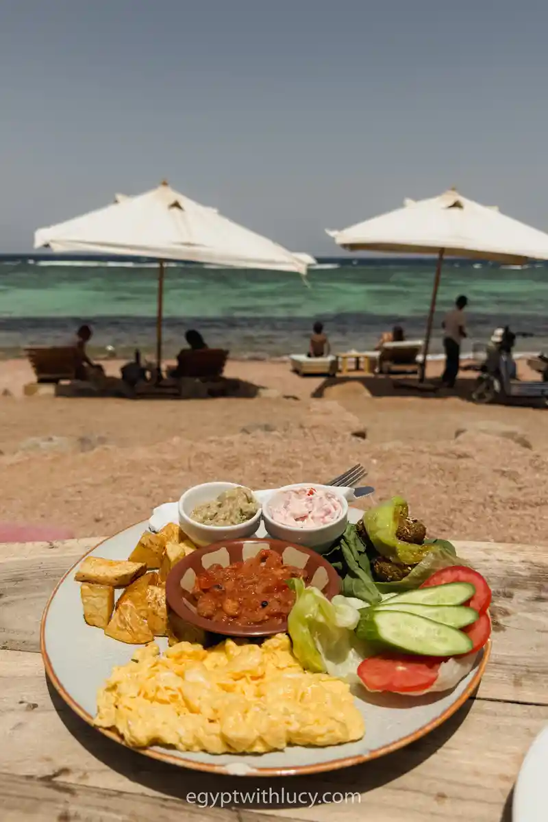 Breakfast plate with eggs, fresh vegetables, potatoes, and small bowls served at a seaside beach.