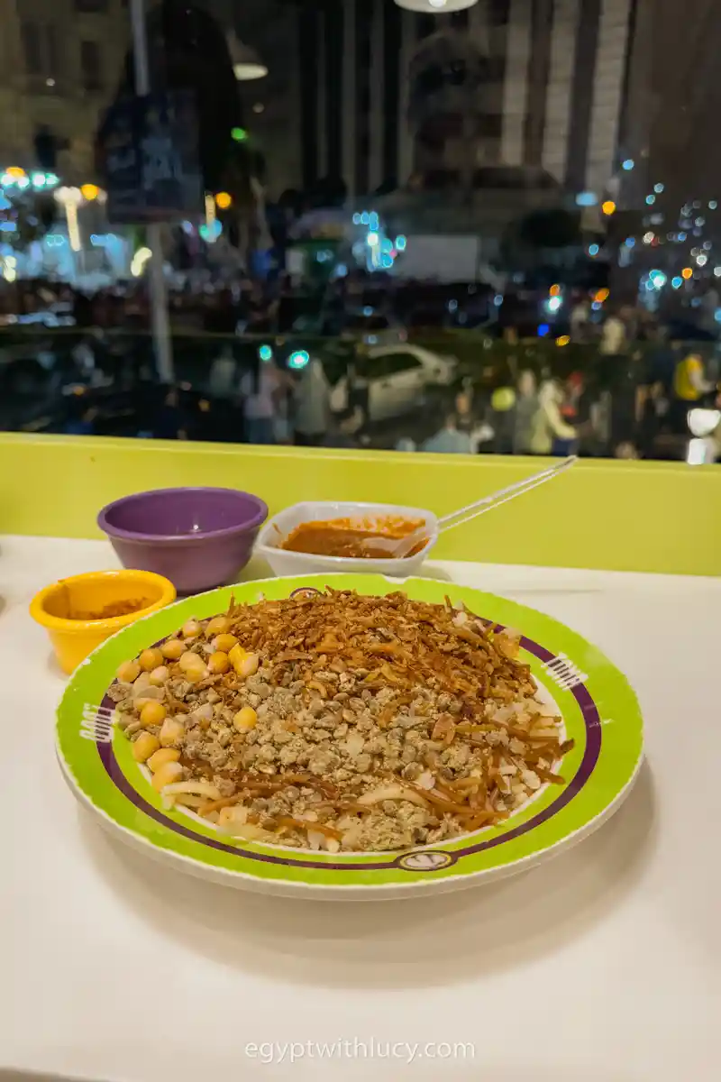 A bowl of traditional Egyptian koshari topped with lentils, chickpeas, and crispy fried onions.