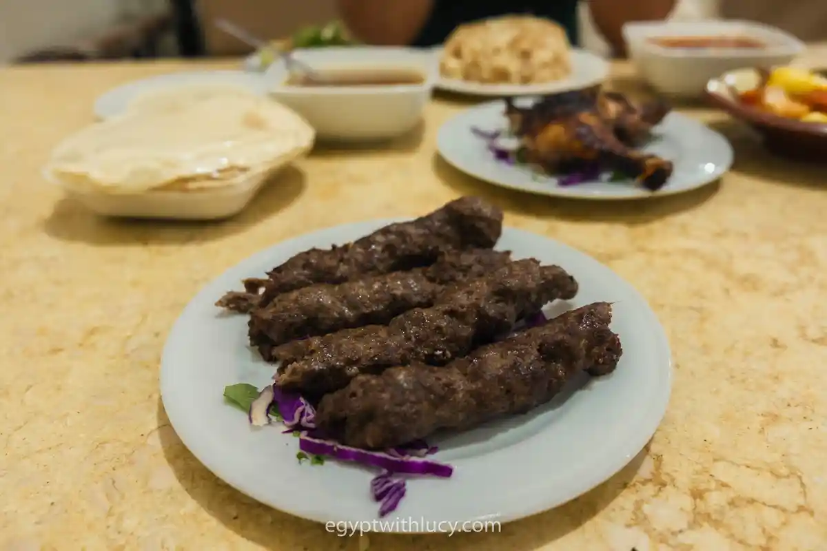 Four grilled minced meat kofta kebabs served over shredded red cabbage on a white plate.