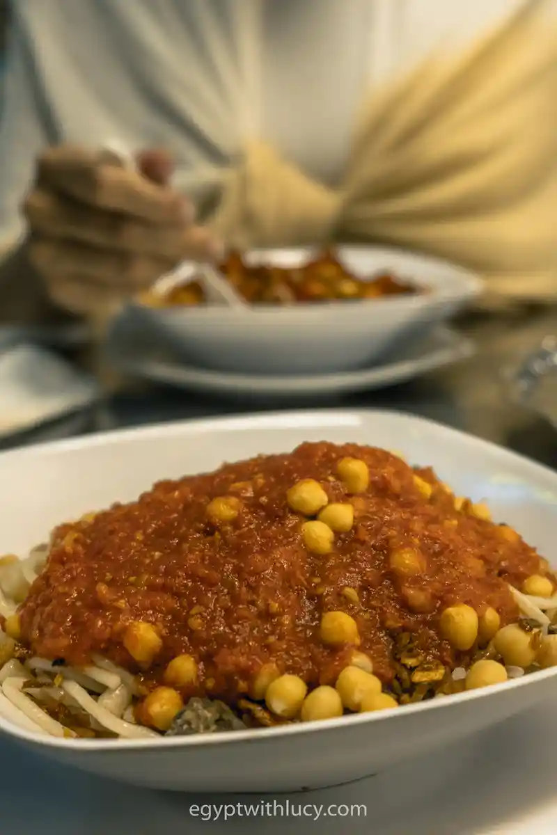 A close-up view of koshari topped with thick tomato sauce and whole yellow chickpeas.