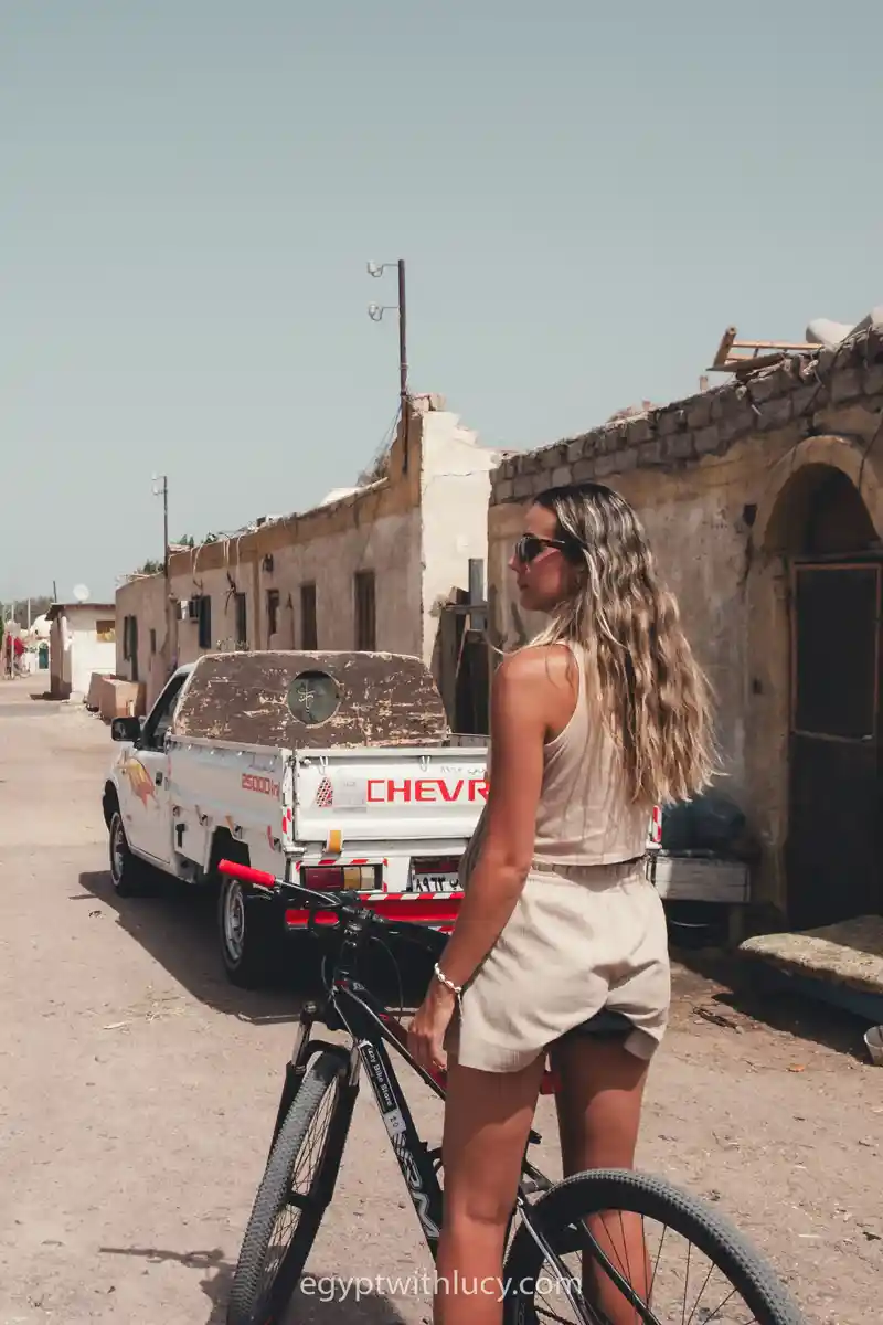Lucy sitting on a bicycle looking back along a dusty street in Assala, Dahab.