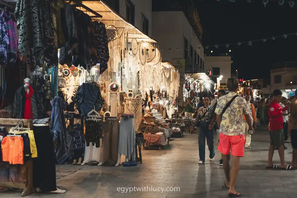 Brightly lit souvenir and clothing shops along a street in Mashraba at night with people walking.