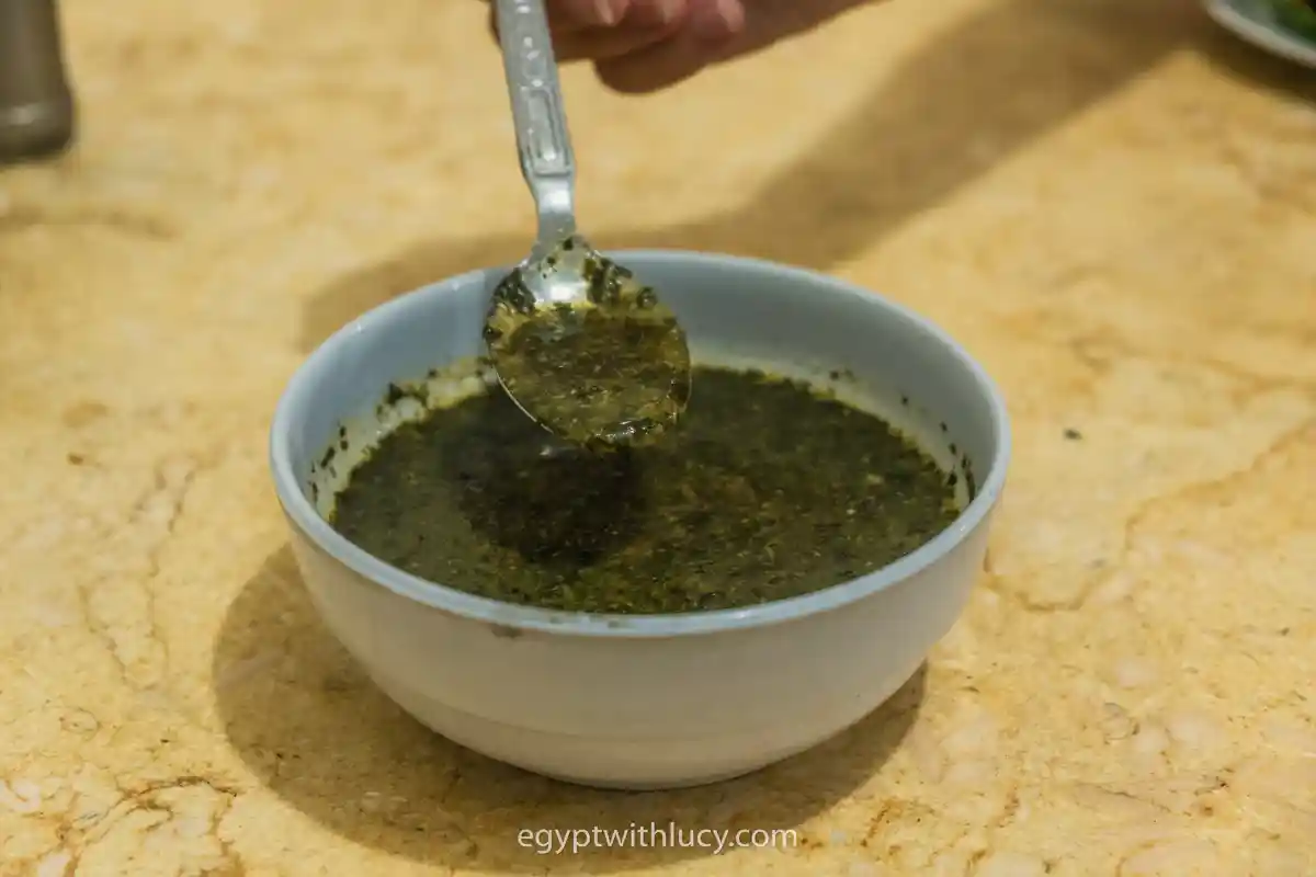 molokhia-egypt A metal spoon lifting dark green molokhia jute leaf soup from a white ceramic bowl.