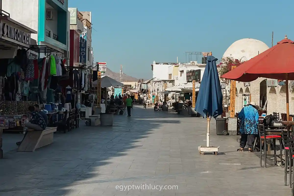 Paved pedestrian street in Mashraba lined with shops, cafes, and outdoor seating under a clear sky.