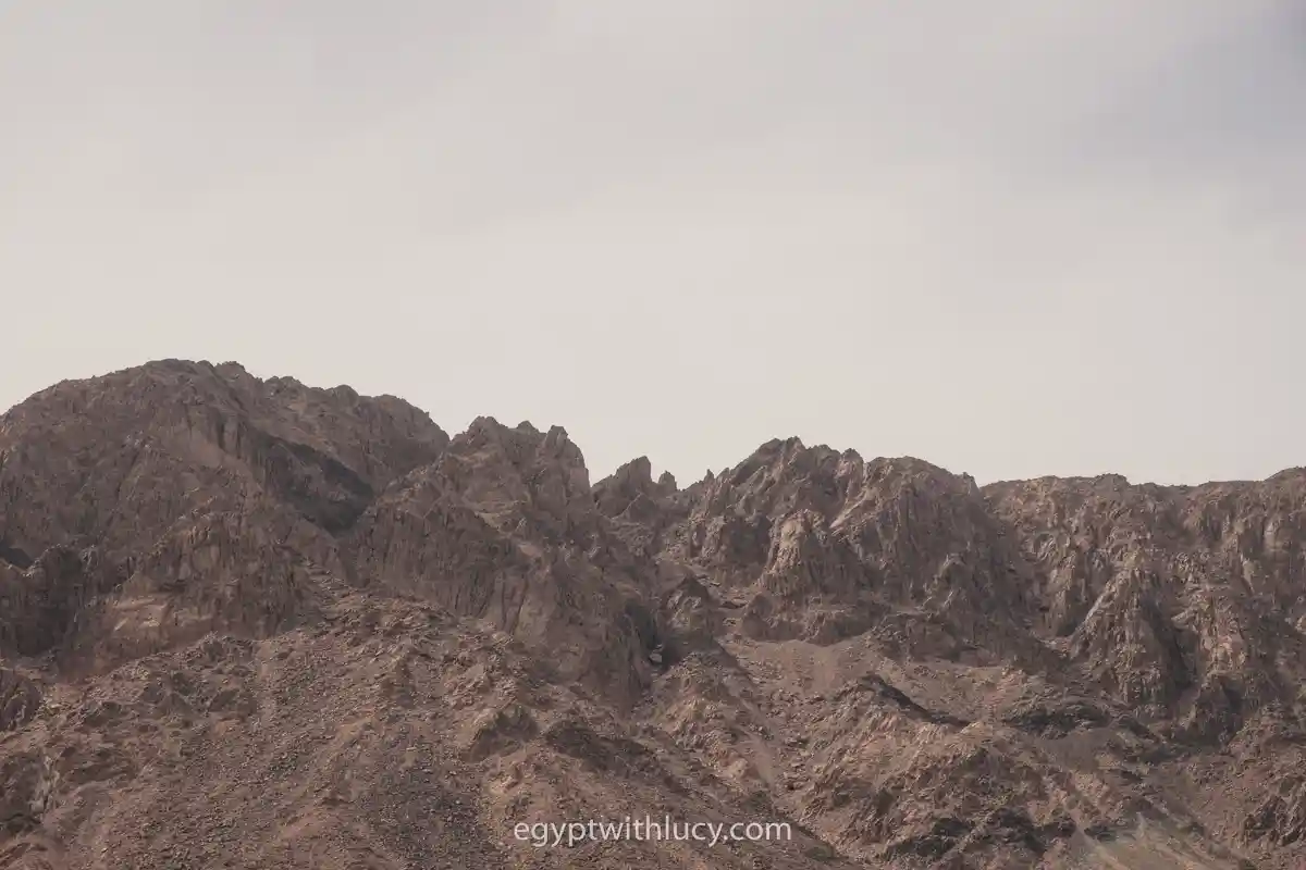 Rugged, rocky mountain peaks stretching across a hazy desert sky.