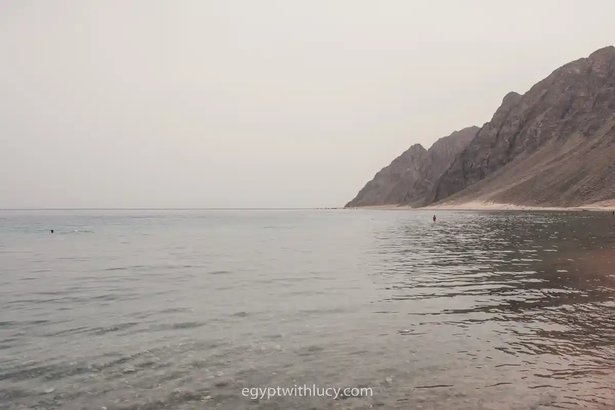 three-pools-overcast Steep coastal mountains rising sharply from a calm, wide expanse of sea water.