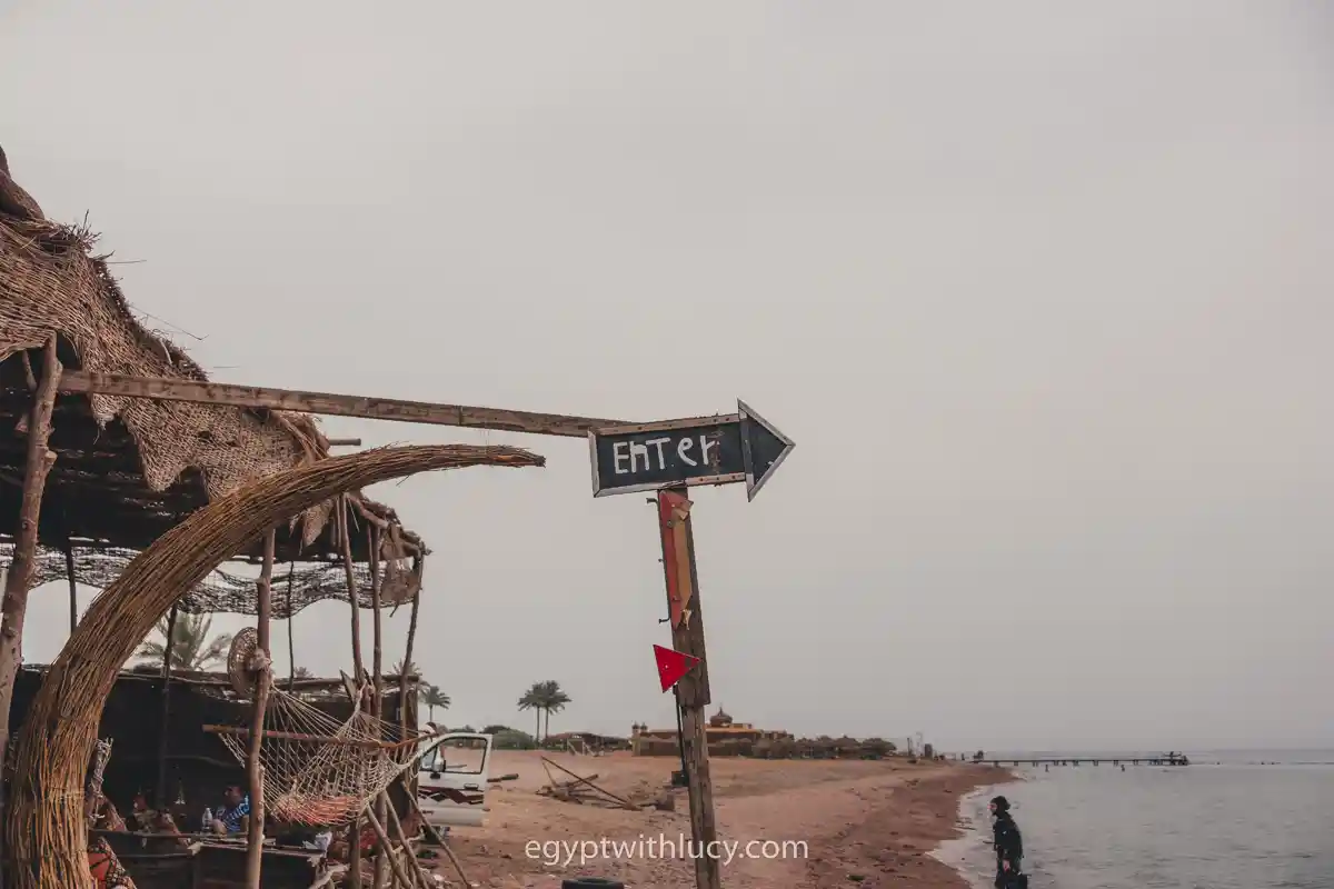 A wooden sign reading "ENTER" pointing toward the beach near a thatched shelter.