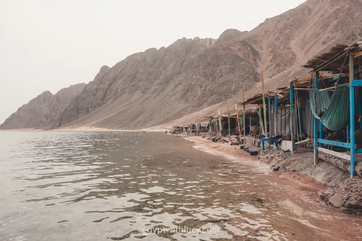 Wooden beach huts with blue posts and green hammocks lining the Three Pools shoreline.