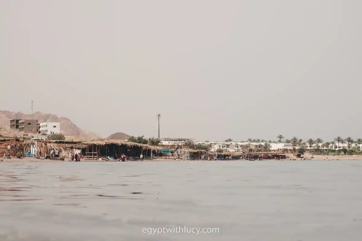 Low-angle view of a distant sandy beach lined with simple waterfront huts.